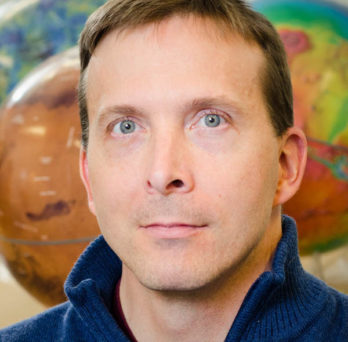 Headshot of Andrew Dombard in front of some spherical planetary models 