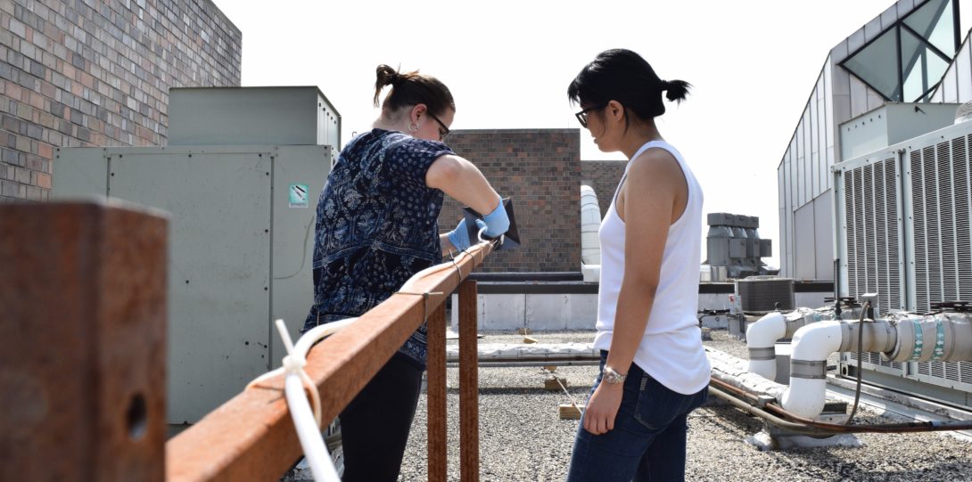Two females on the roof of a building collecting data.