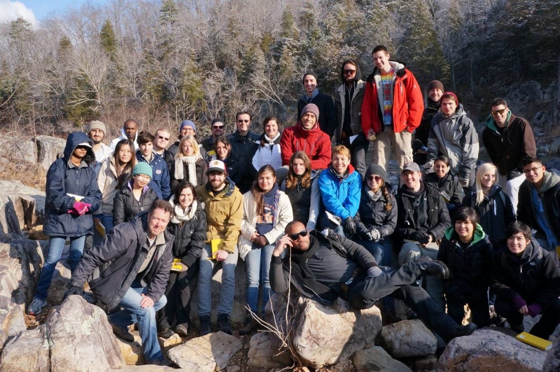 Group photo in outdoor setting with rocks in the front and branched tress in the background.