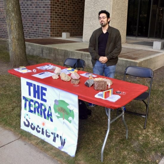 Geoscience student at a table outside with lots of rock specimens on it.