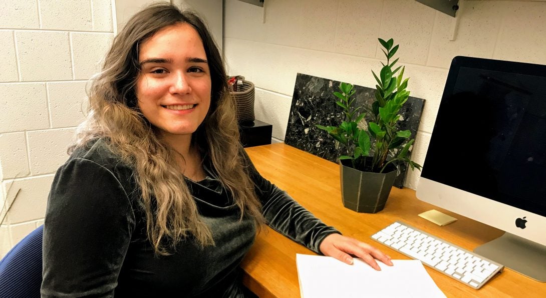 Kala Badillo sitting in front of a desk with a computer and paleontology textbook 