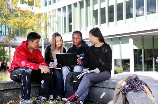 Image of a diverse group of 4 students sitting outside looking at a laptop.