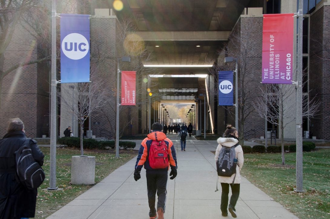 Students outside walking in between two buildings.  UIC in blue and red ombre are on the sides of the sidewalk