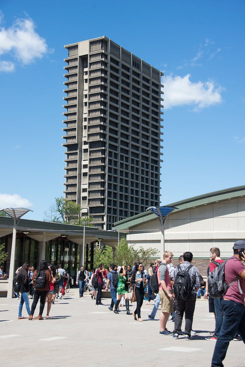 Tall concrete building, UIC's University Hall, with blue sky in the background and students in foreground.